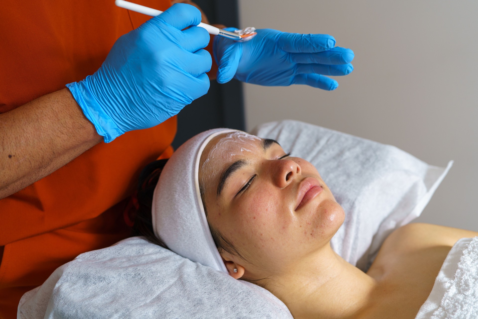 Beautician applying a facial mask on a young asian woman's forehead