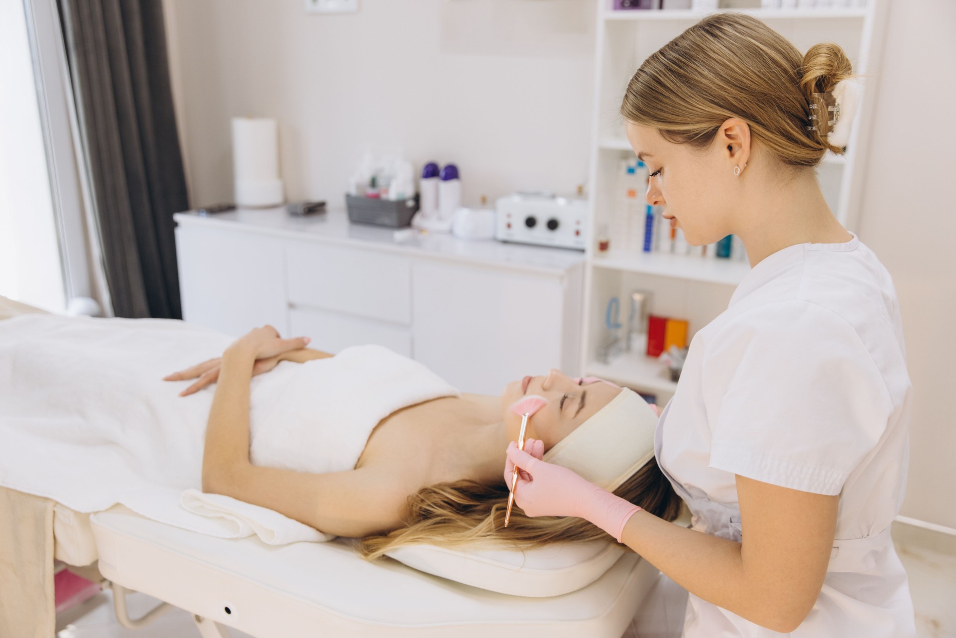 Professional beautician performing facial treatment on relaxed woman during skincare session at modern beauty center